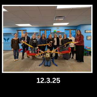 A group of people gathers in a blue-walled room for a ribbon-cutting ceremony, holding a large golden pair of scissors.