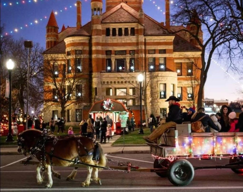 The Williams County Courthouse in the background with a wagon decorated in Christmas lights being pulled by a horse.