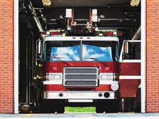 Firetruck in the fire station with the garage door open.
