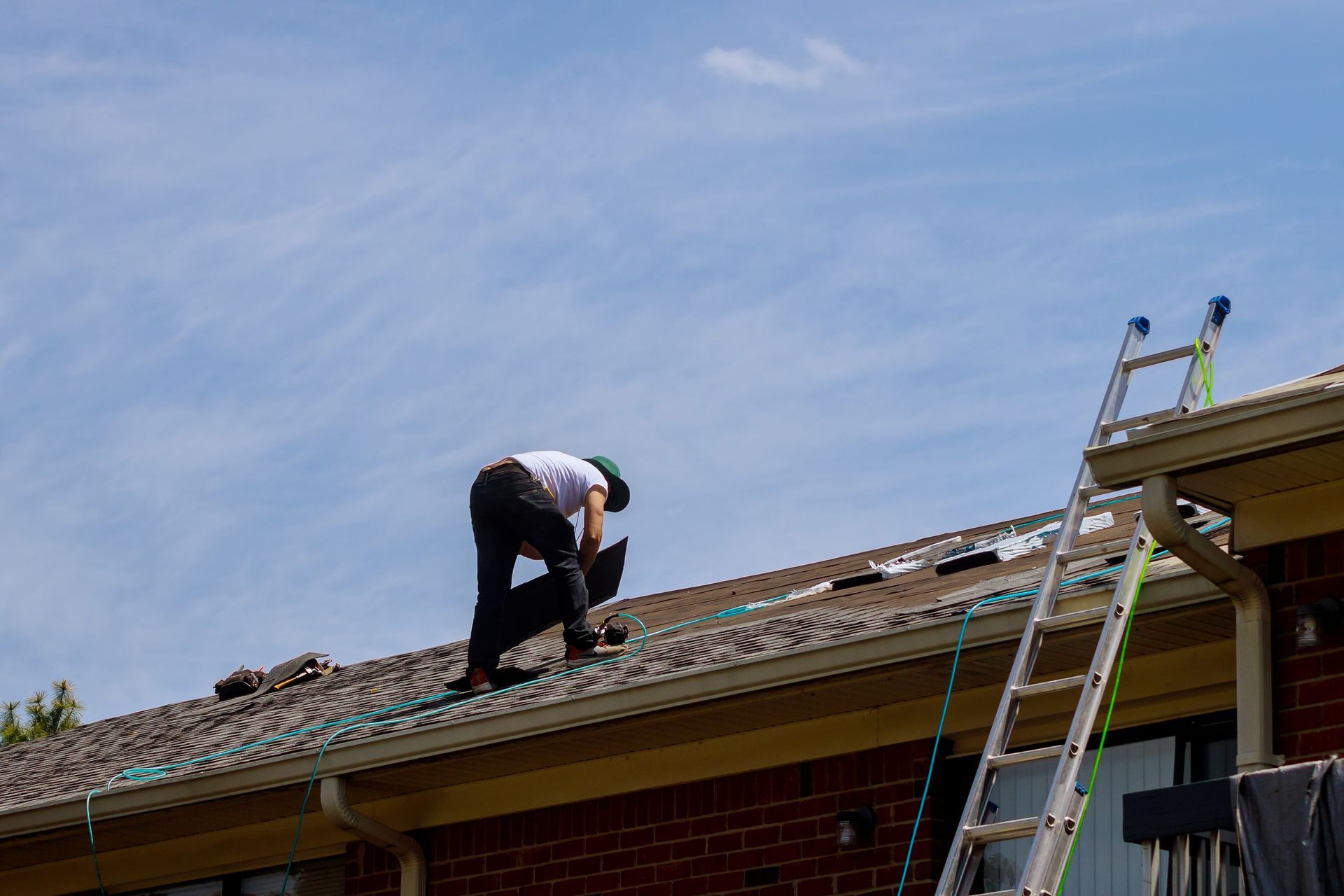 a man is working on the roof for repair of a building next to a ladder .
