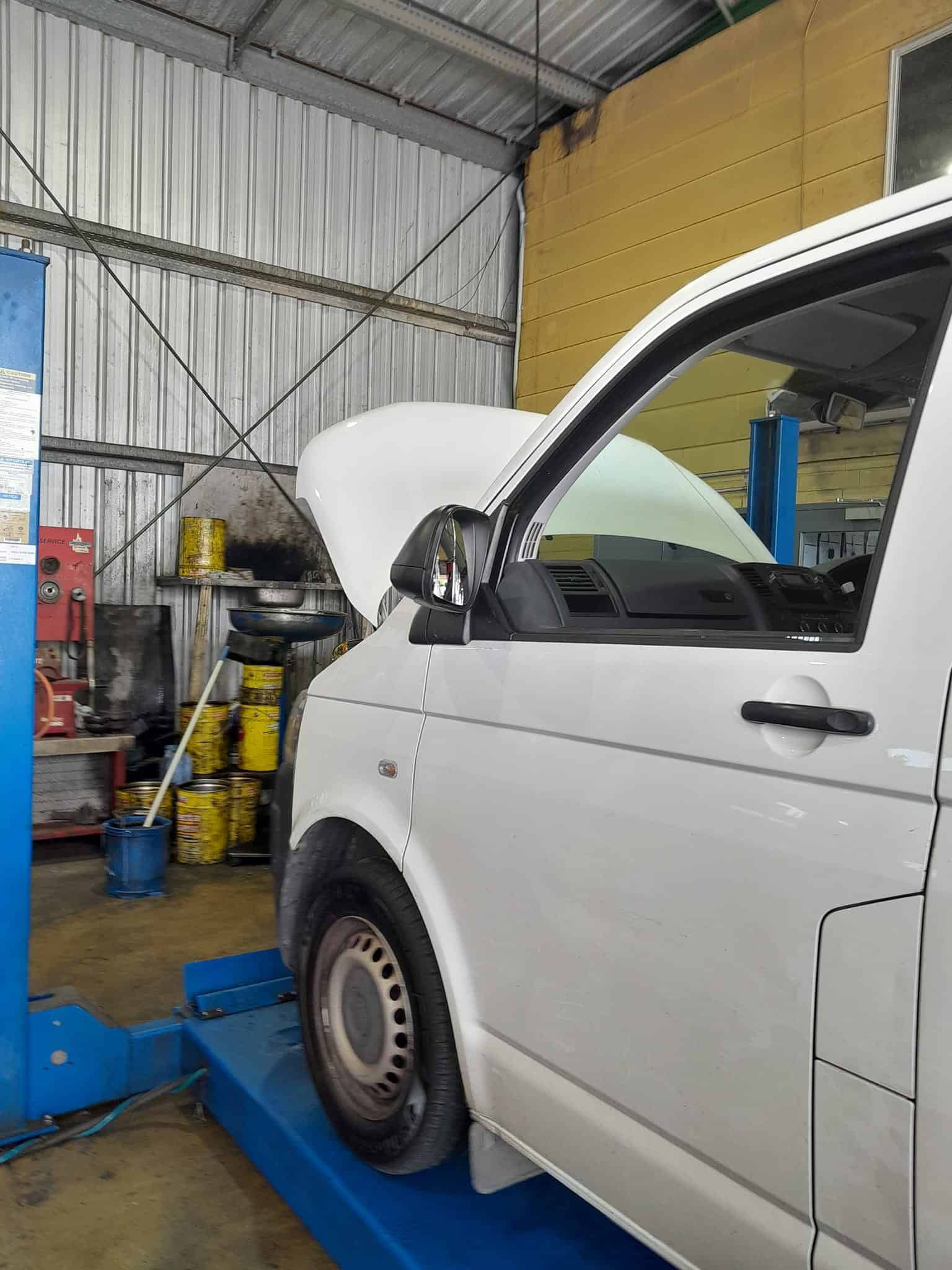 A White Van With the Hood Up is Sitting on a Lift in a Garage — CB Automotive In Yatala, QLD
