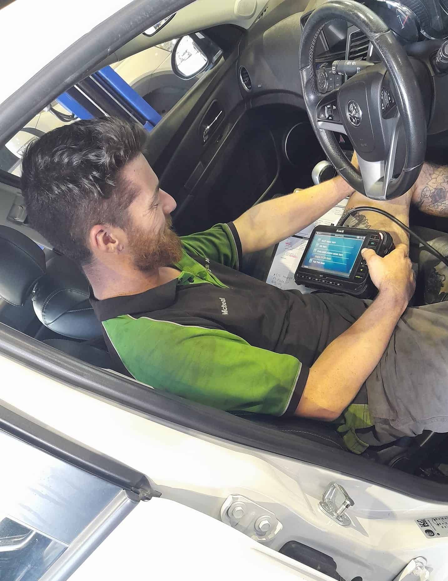 A Man is Sitting in the Driver 's Seat of a Car Using a Tablet — CB Automotive In Yatala, QLD