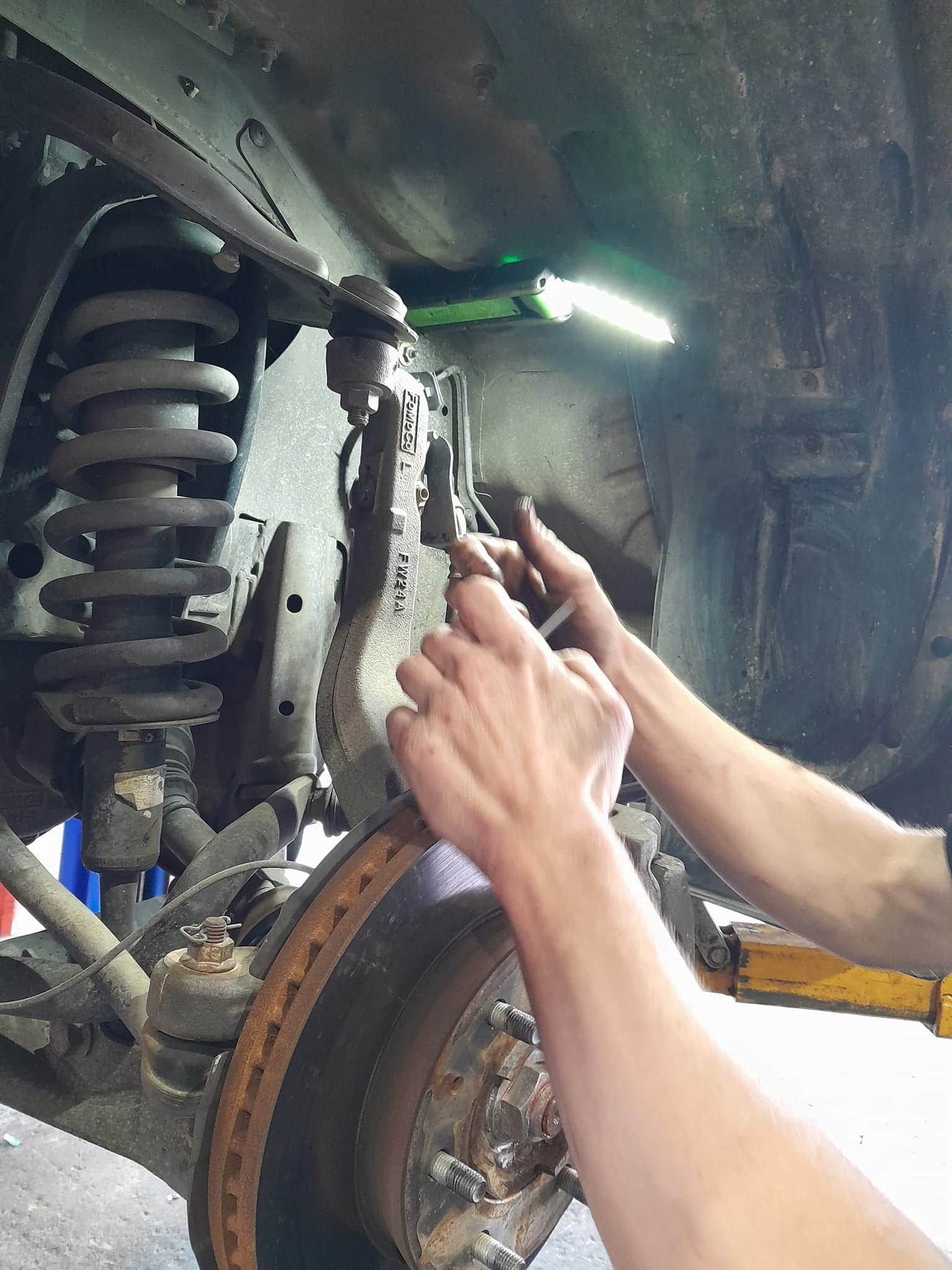 A person is working on the suspension of a car. — CB Automotive In Yatala, QLD