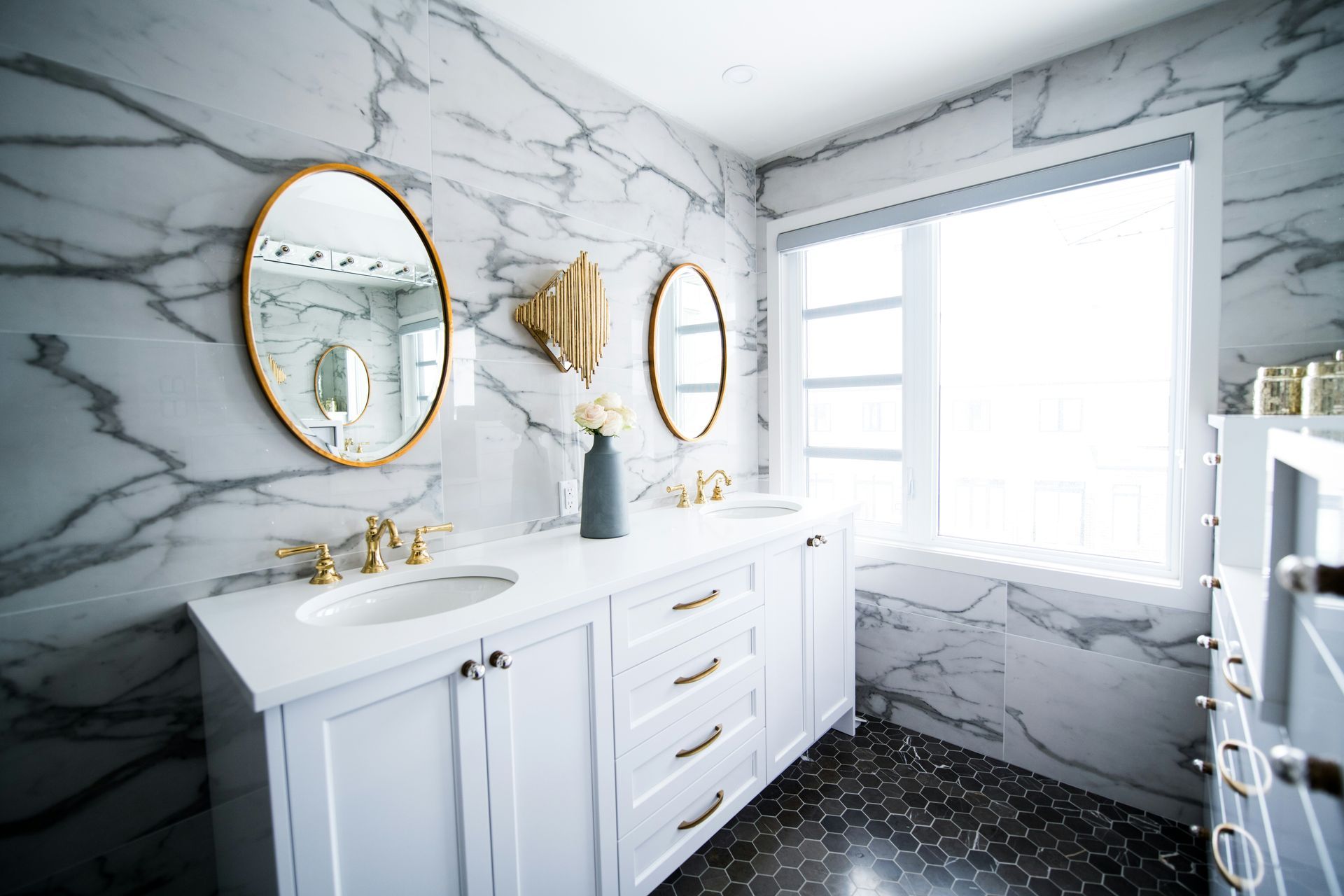 A bathroom with two sinks , two mirrors and a window.