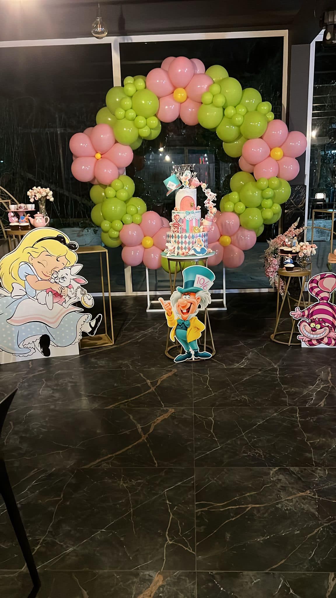 Decorazioni per feste a tema Alice nel Paese delle Meraviglie. Include torta, ghirlanda di palloncini, sagome dei personaggi e tavoli.