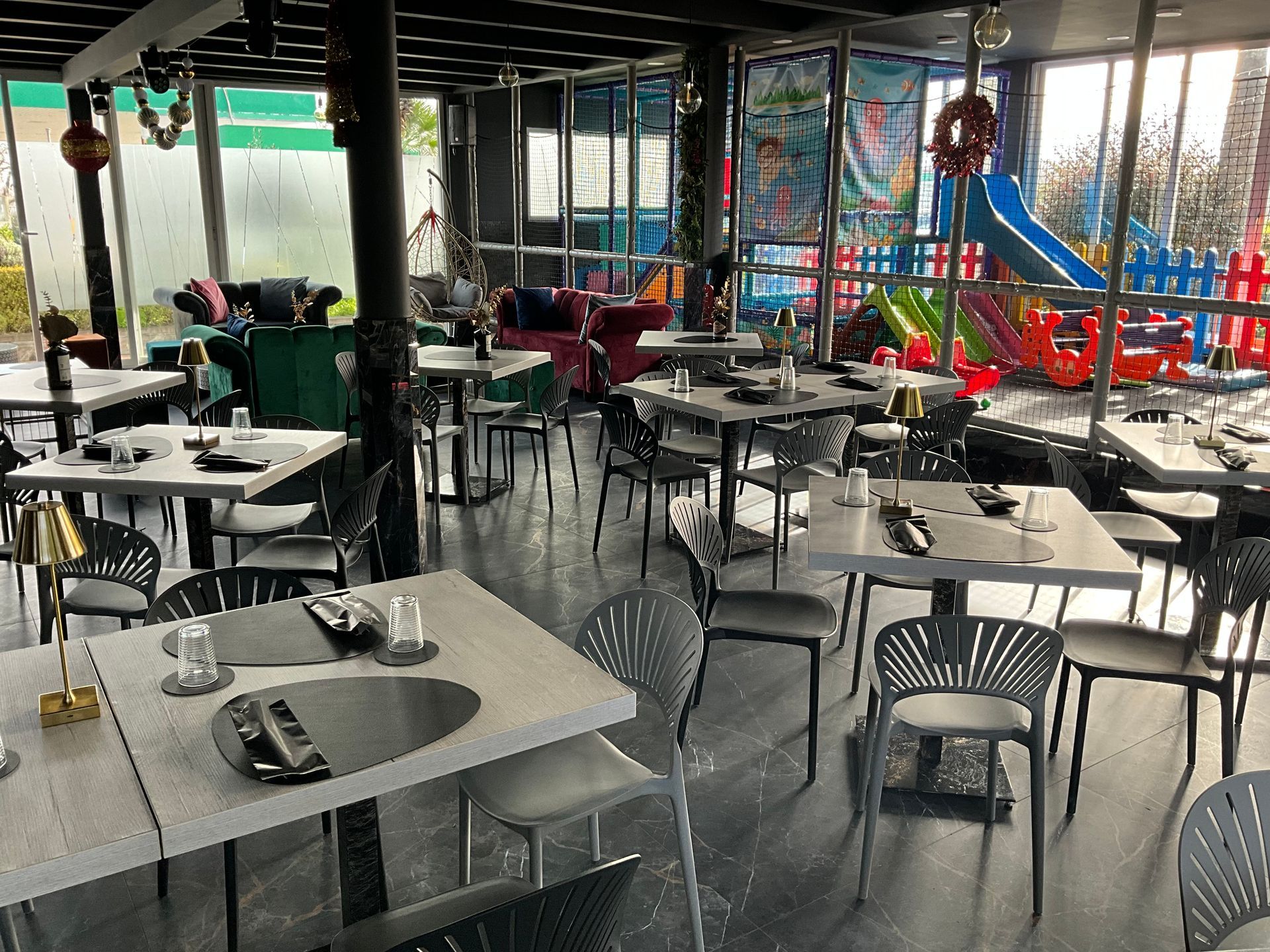 Interno del ristorante con tavoli, sedie e un'area giochi per bambini visibile attraverso le finestre.