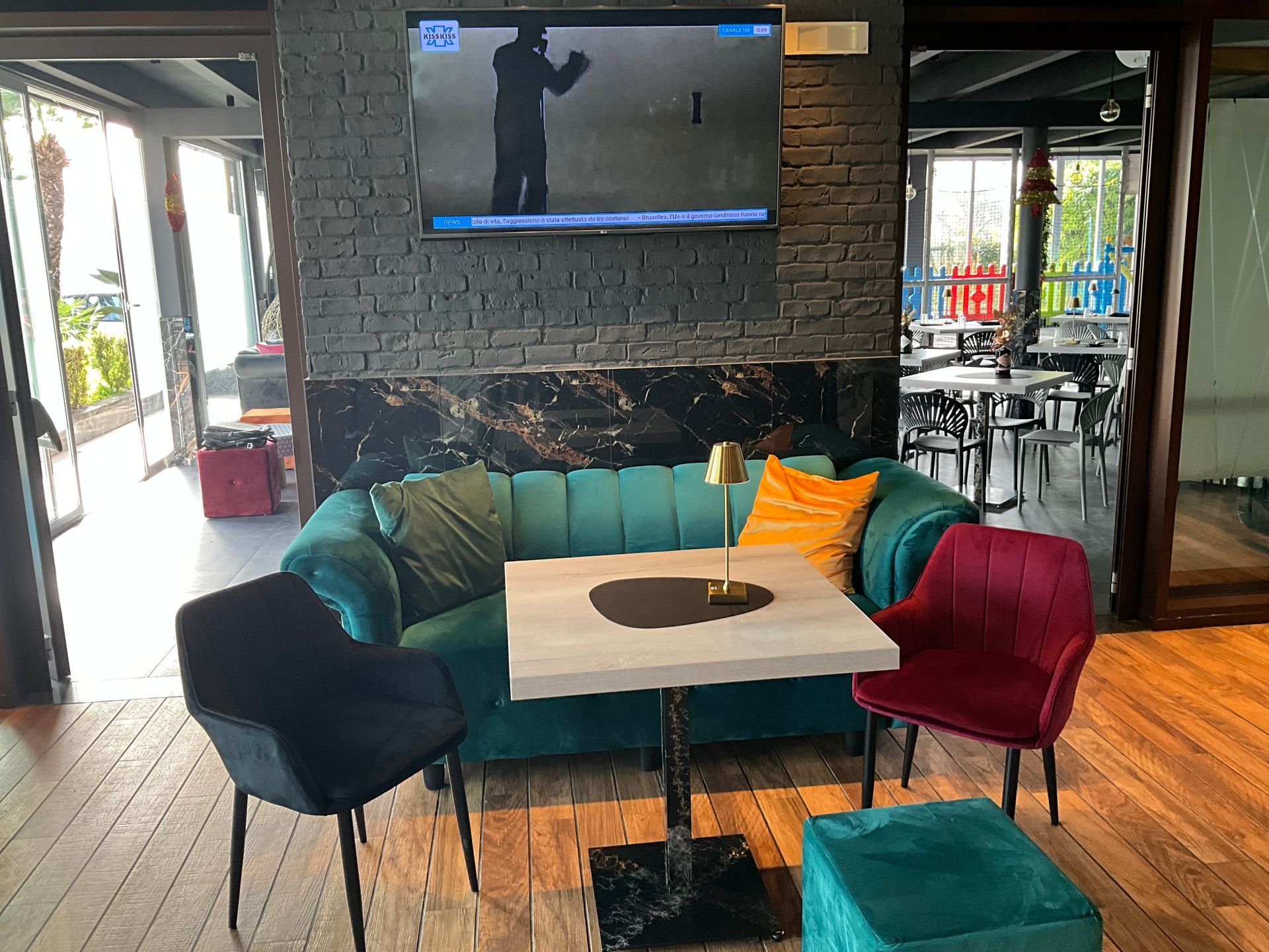 Un divano e delle sedie color verde acqua in un ambiente da bar, con un televisore acceso sopra un tavolino.
