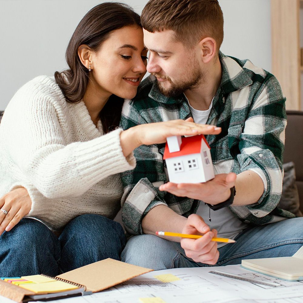 A man and a woman are sitting on the floor looking at a model house.