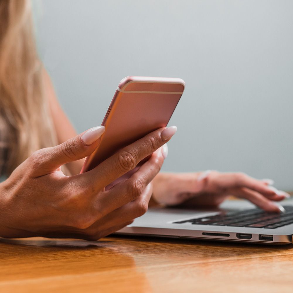 A woman is using a laptop and a cell phone at the same time.
