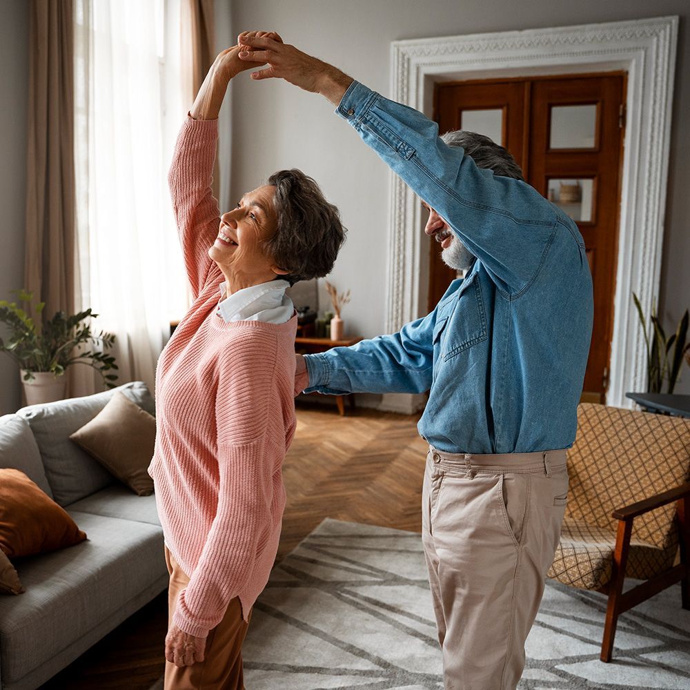An elderly couple is dancing together in a living room.