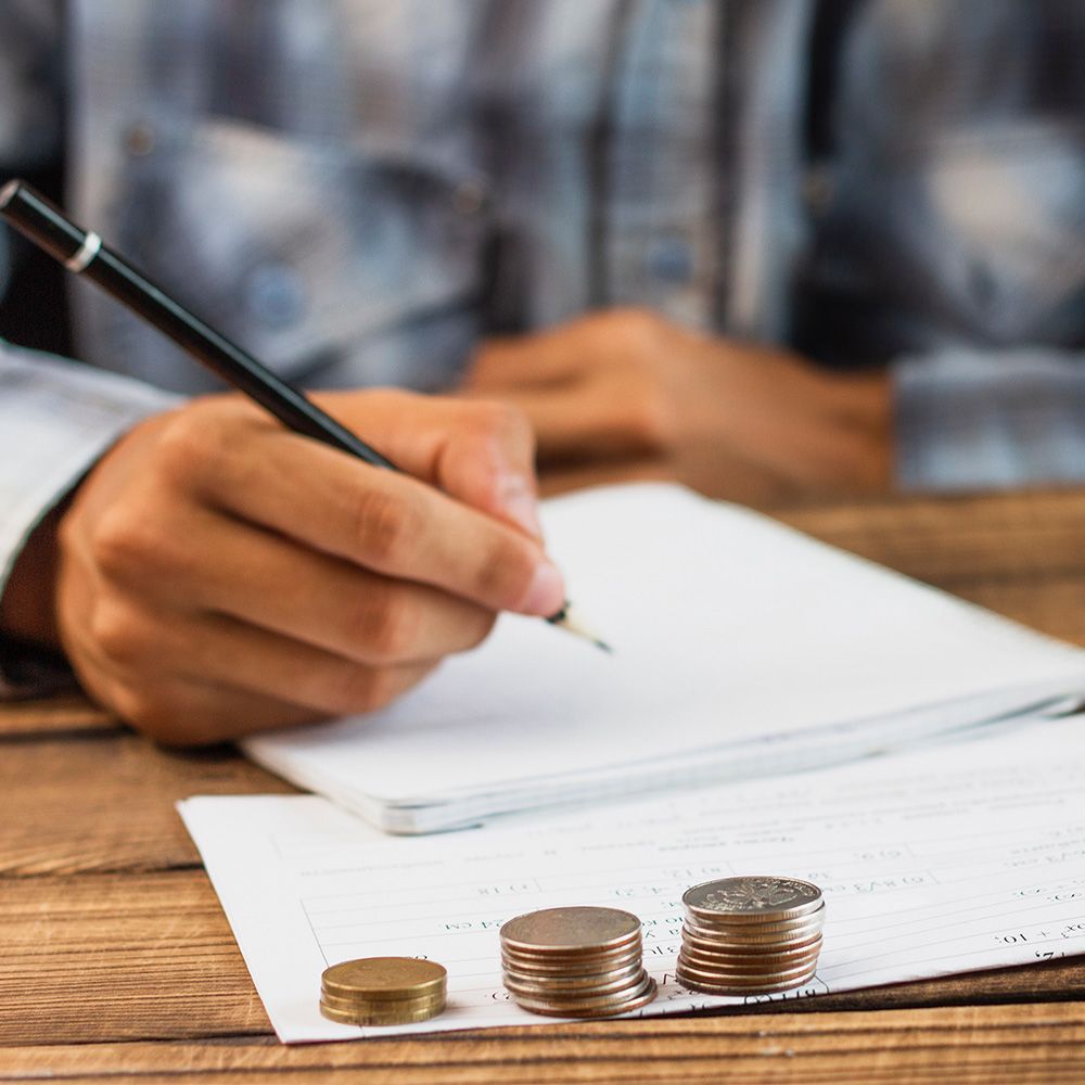 A person is writing on a piece of paper next to stacks of coins.