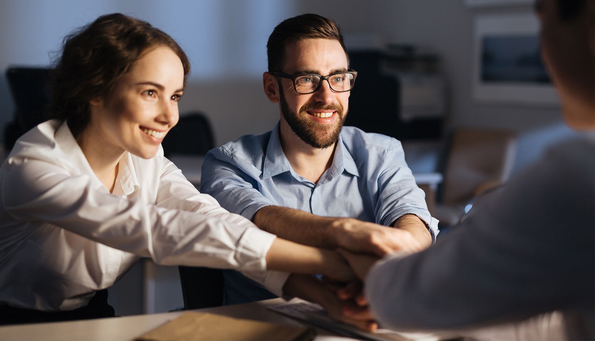 A man and a woman are shaking hands while sitting at a table.