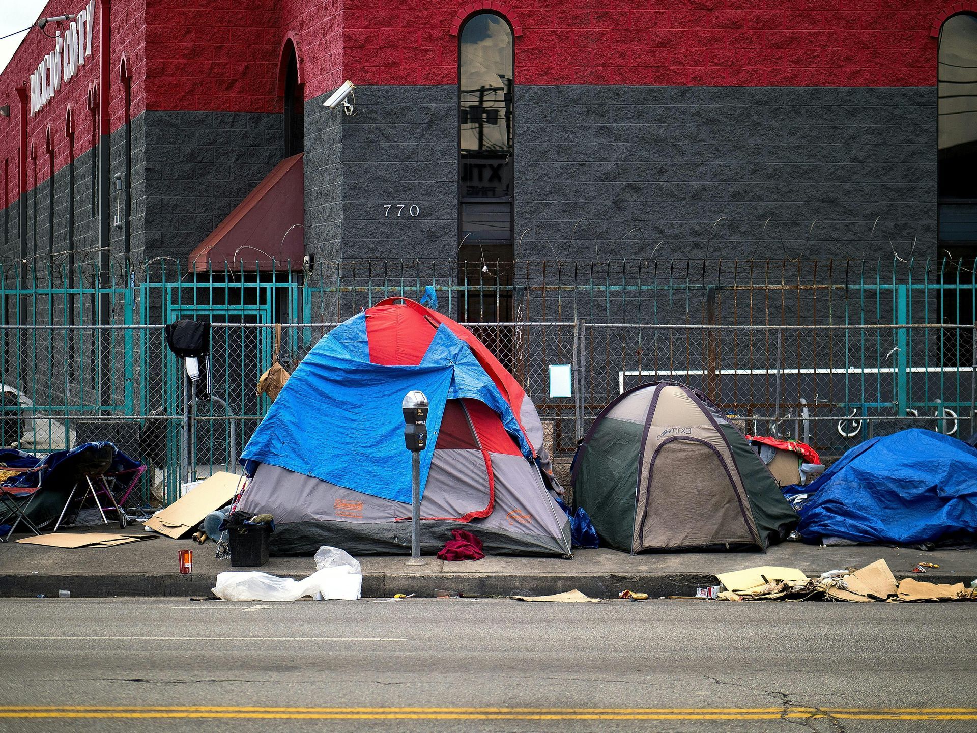 Tents and debris line the sidewalk in front of a brick building.