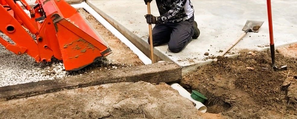 A man working on gravel driveway drainage with shovel and backhoe