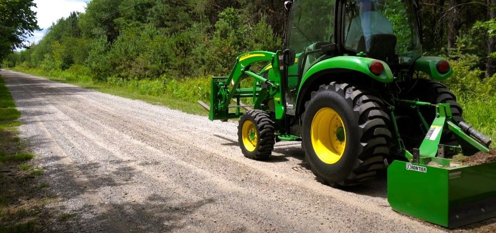 A green and yellow tractor parked beside a gravel road in a forested area.