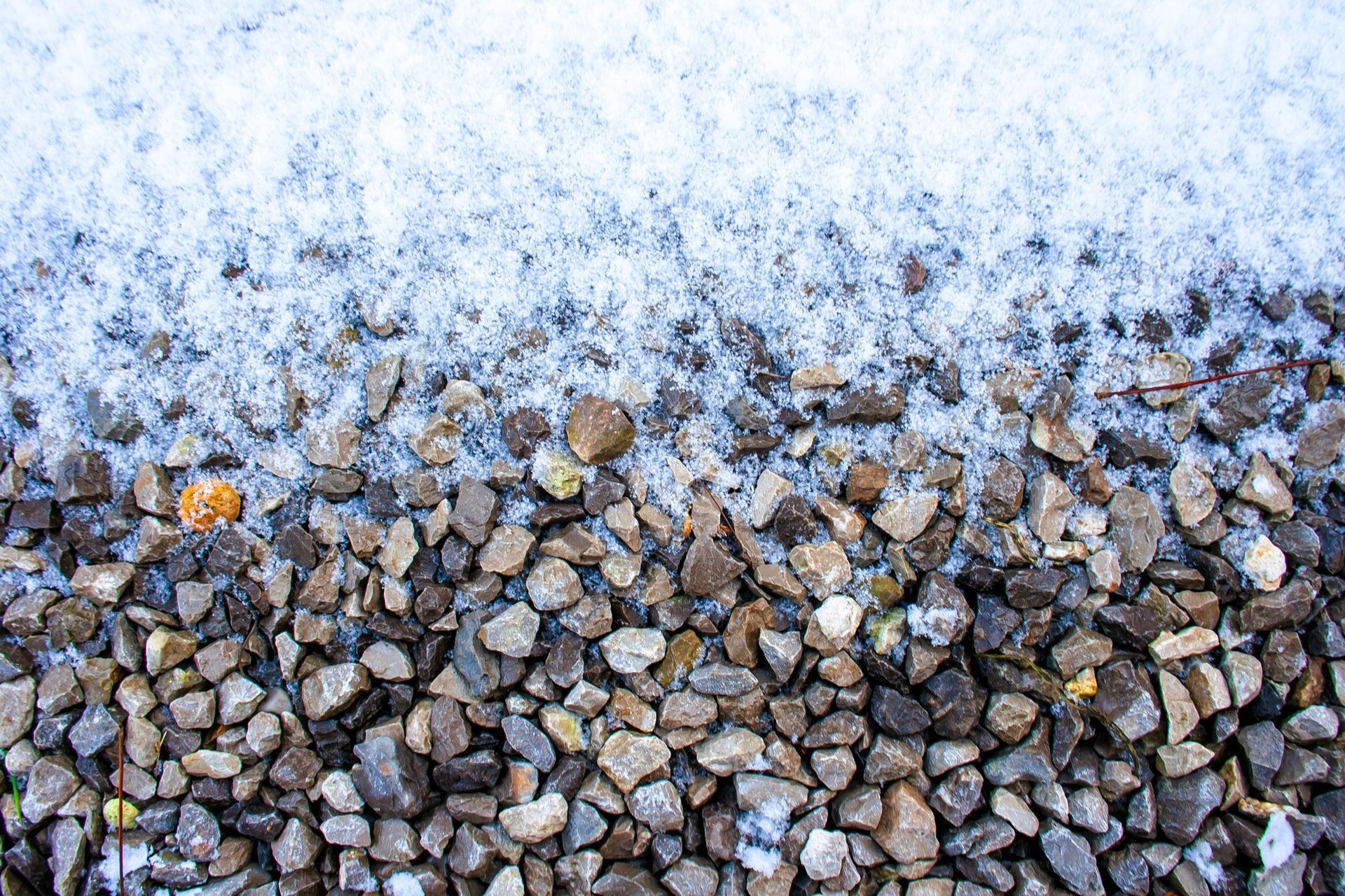 Snow-covered gravel road with frosty pebbles and a winter landscape.