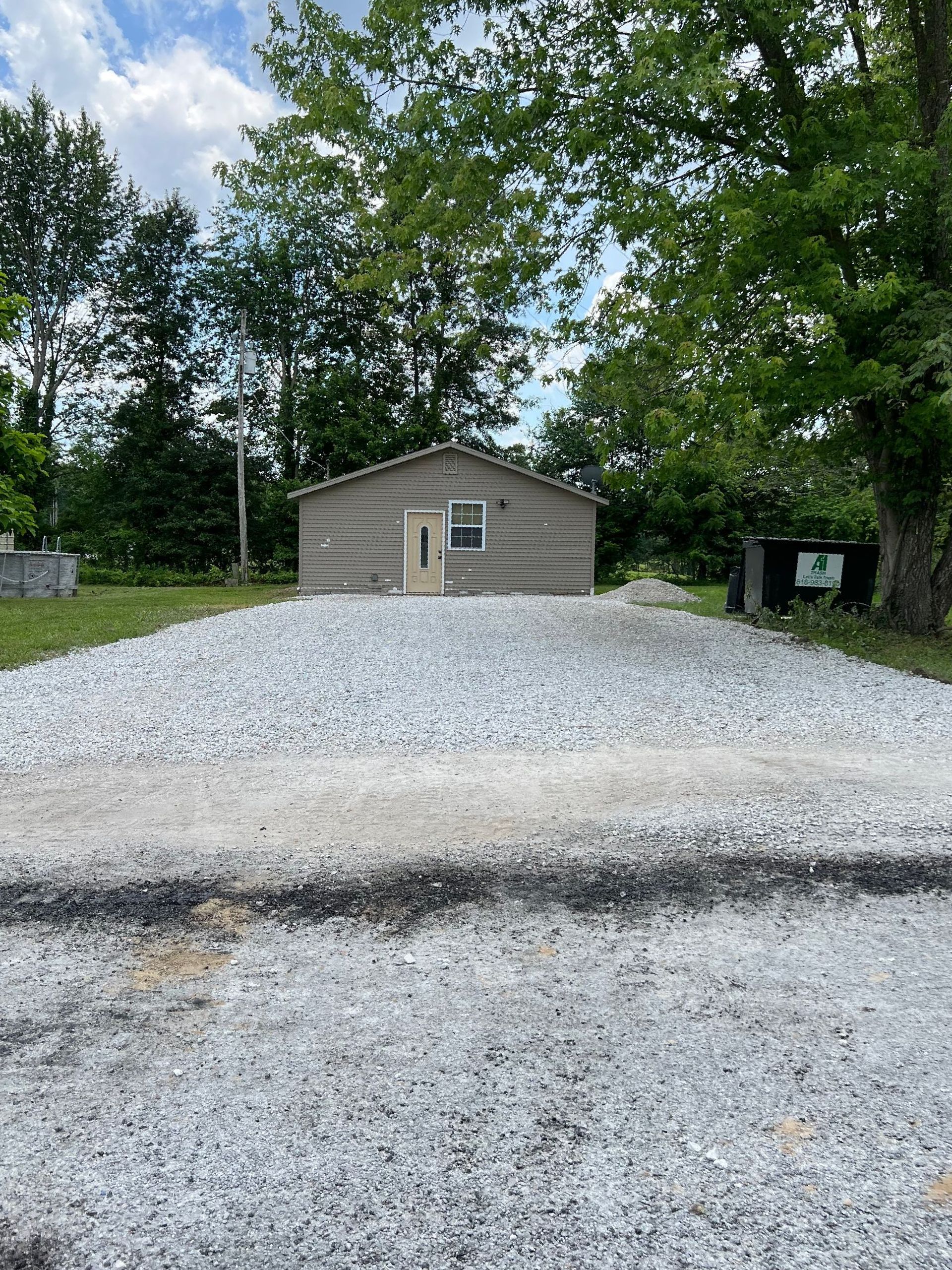 A small house is sitting at the end of a gravel driveway.