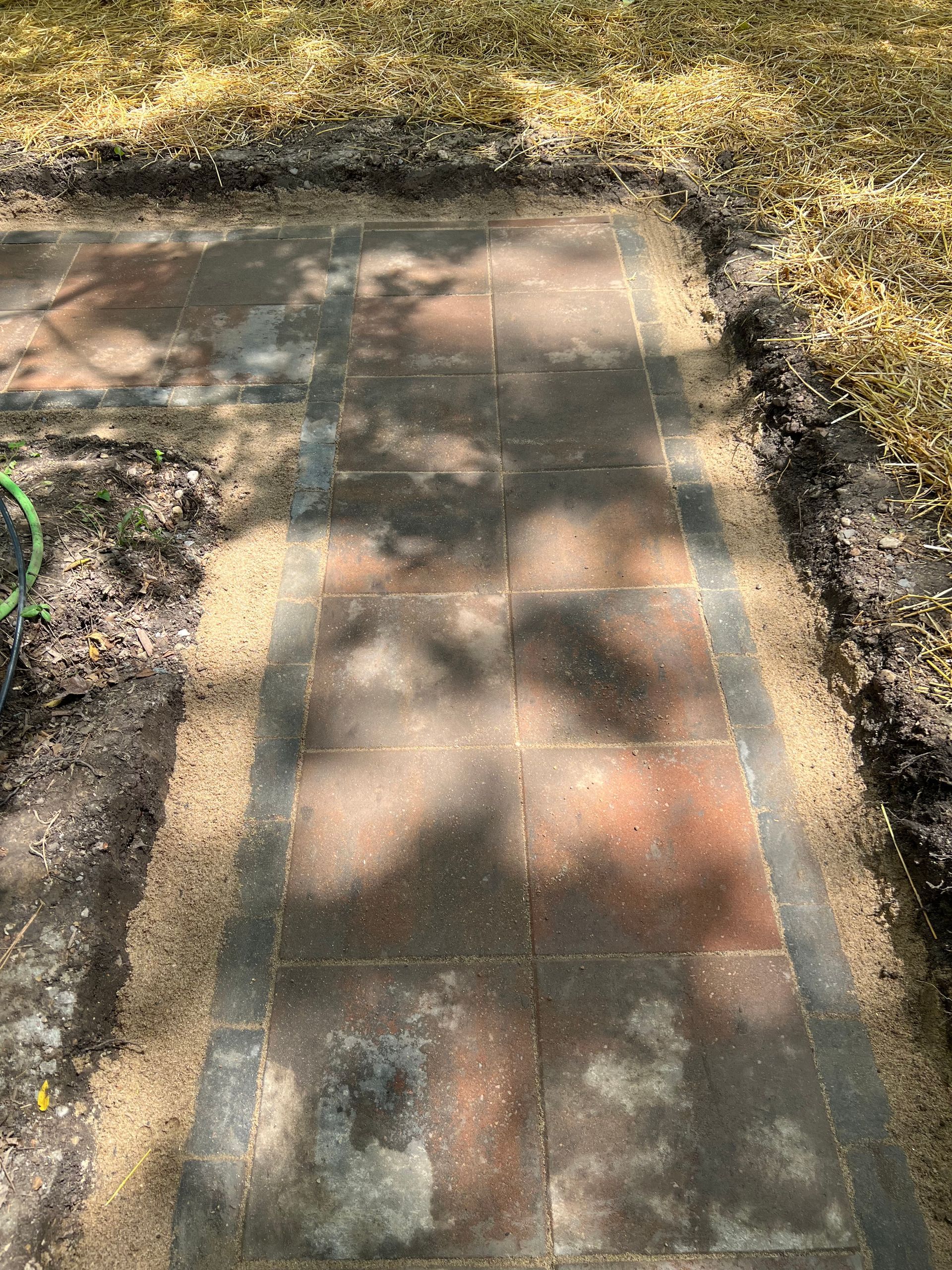 A brick walkway is being built in a backyard.