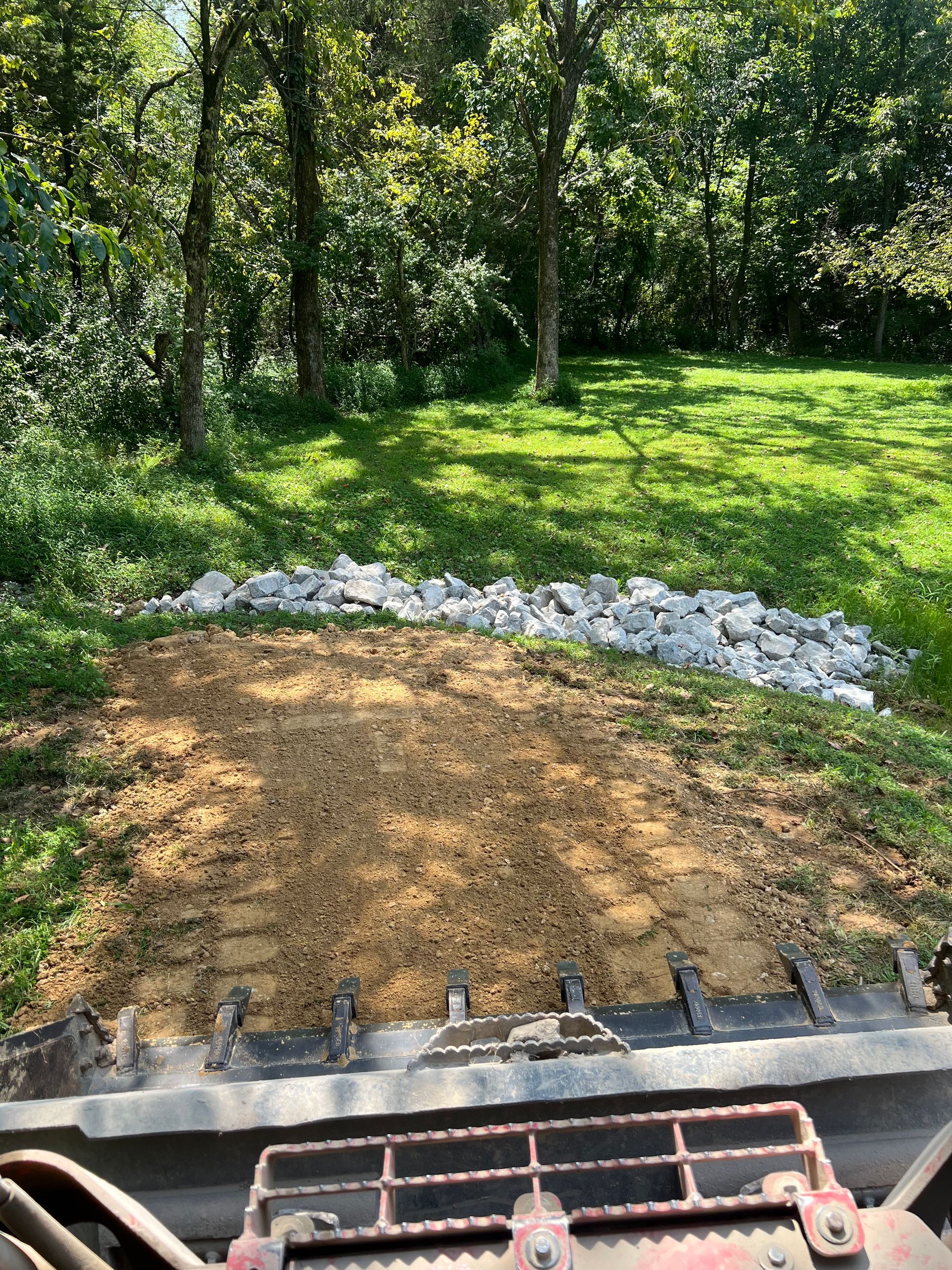 A bulldozer is grading a yard with trees in the background.