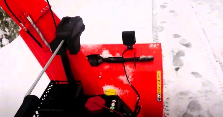 Red snow blower on a snow-covered gravel driveway with footprints to the side