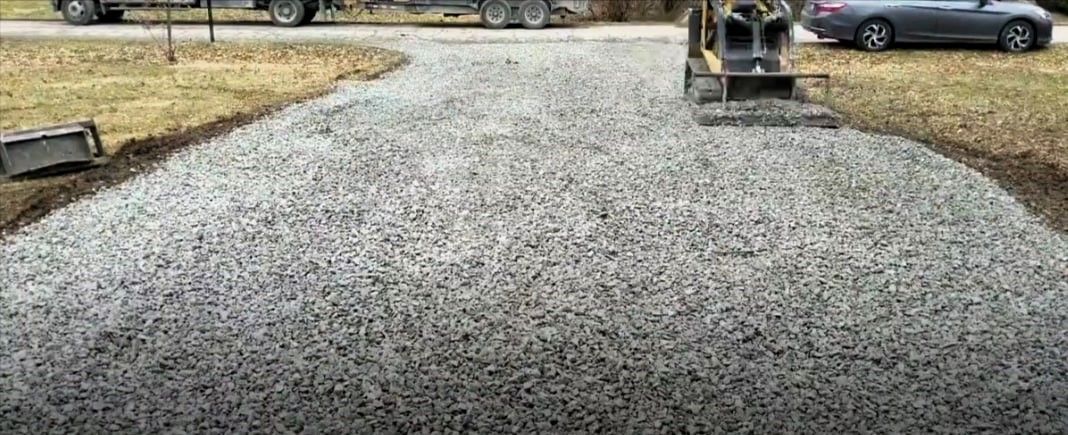 Freshly laid solid gravel driveway with construction equipment and parked cars.