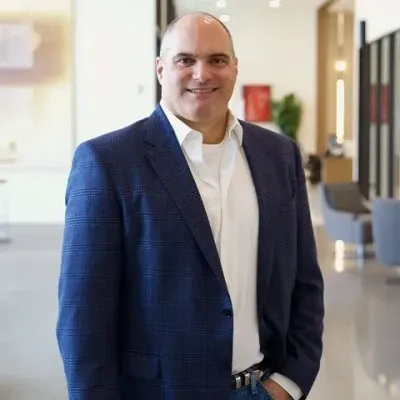 A man in a suit and white shirt is standing with his arms crossed.