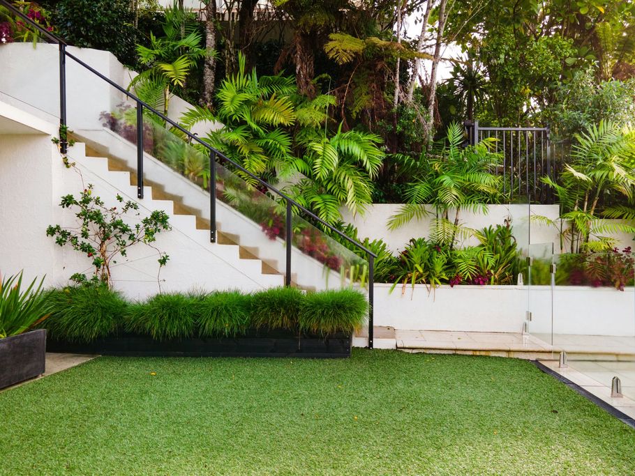 Modern backyard with white terraced steps, lush greenery, and a manicured lawn