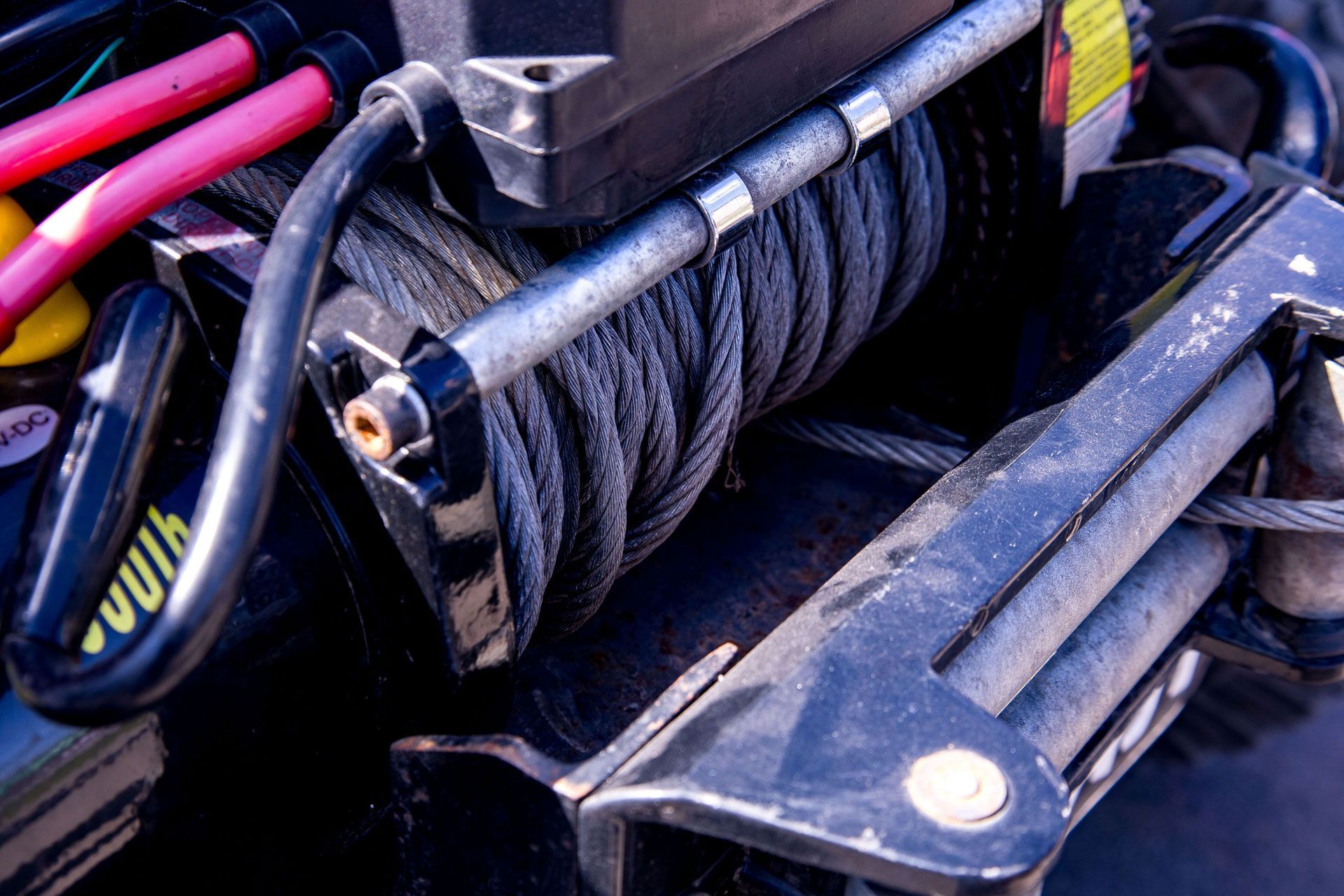 Close-up of a black winch with coiled cable. Red and black cables attached.