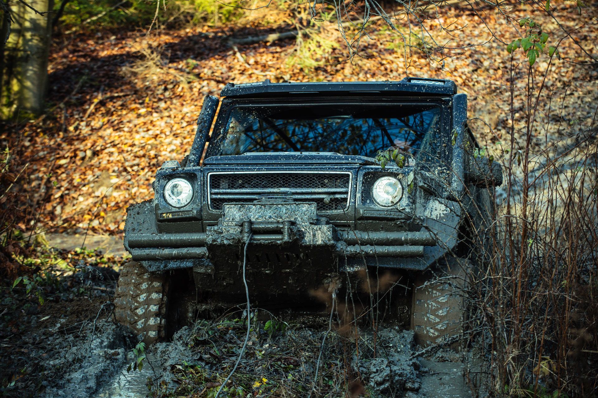 Mud-covered black off-road vehicle driving through muddy terrain in a wooded area.