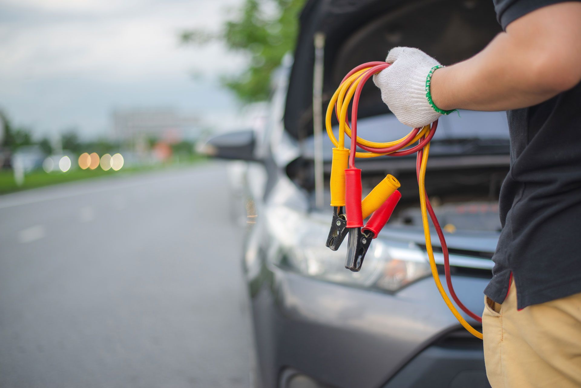 Person holding jumper cables near a car with the hood open.