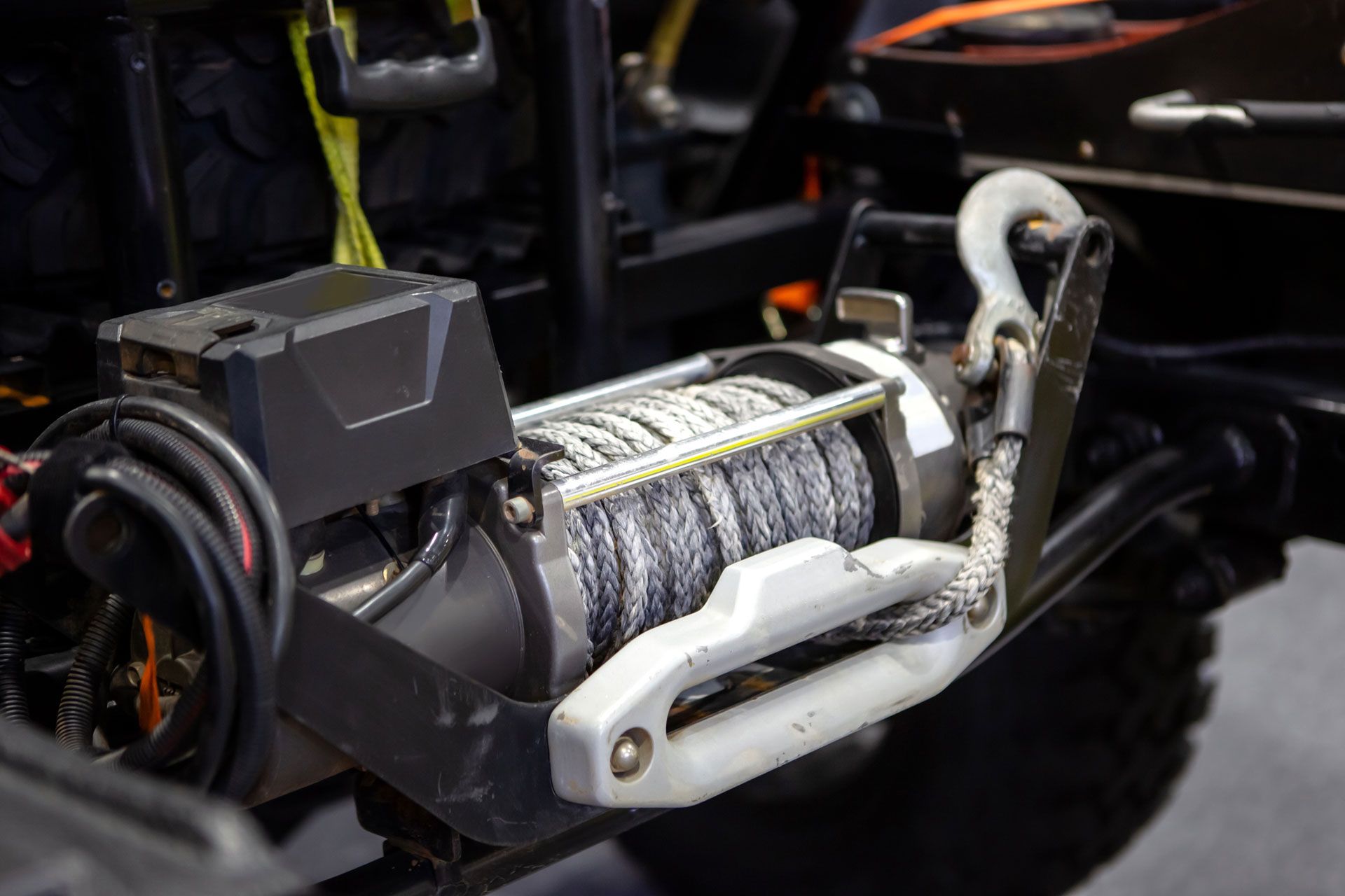 A black winch mounted on a vehicle, with a cable extending to a hook.