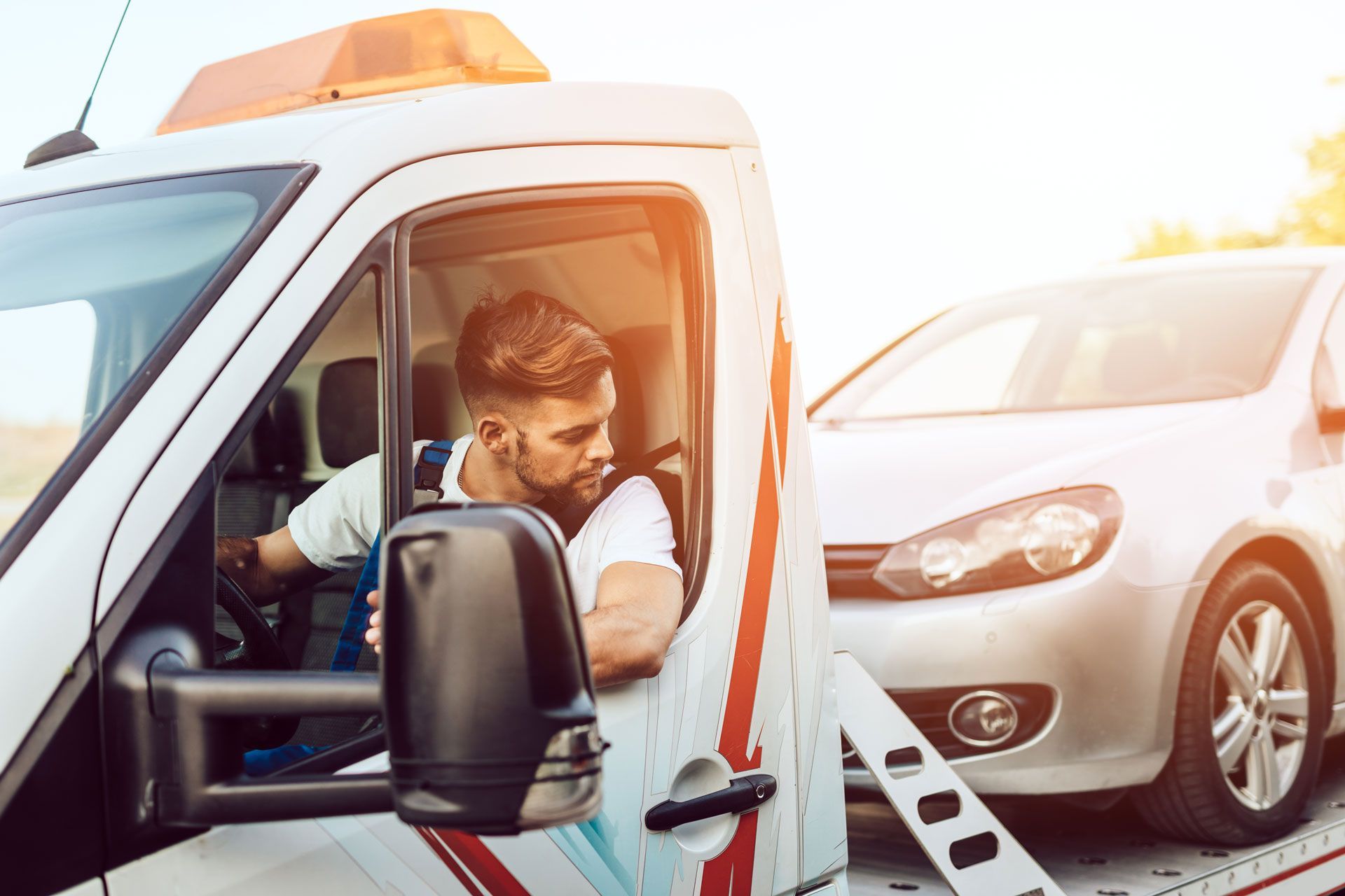 Tow truck operator preparing to tow a silver car on a sunny day.