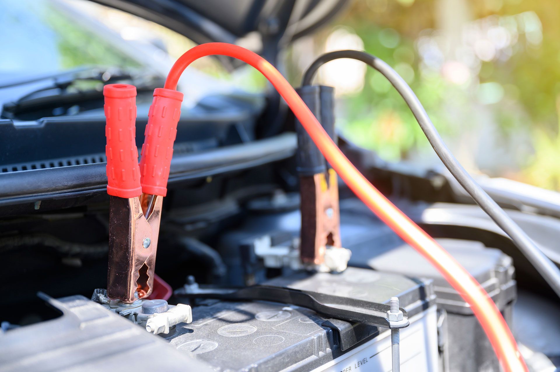 Red and black jumper cables connected to a car battery to jumpstart the vehicle.