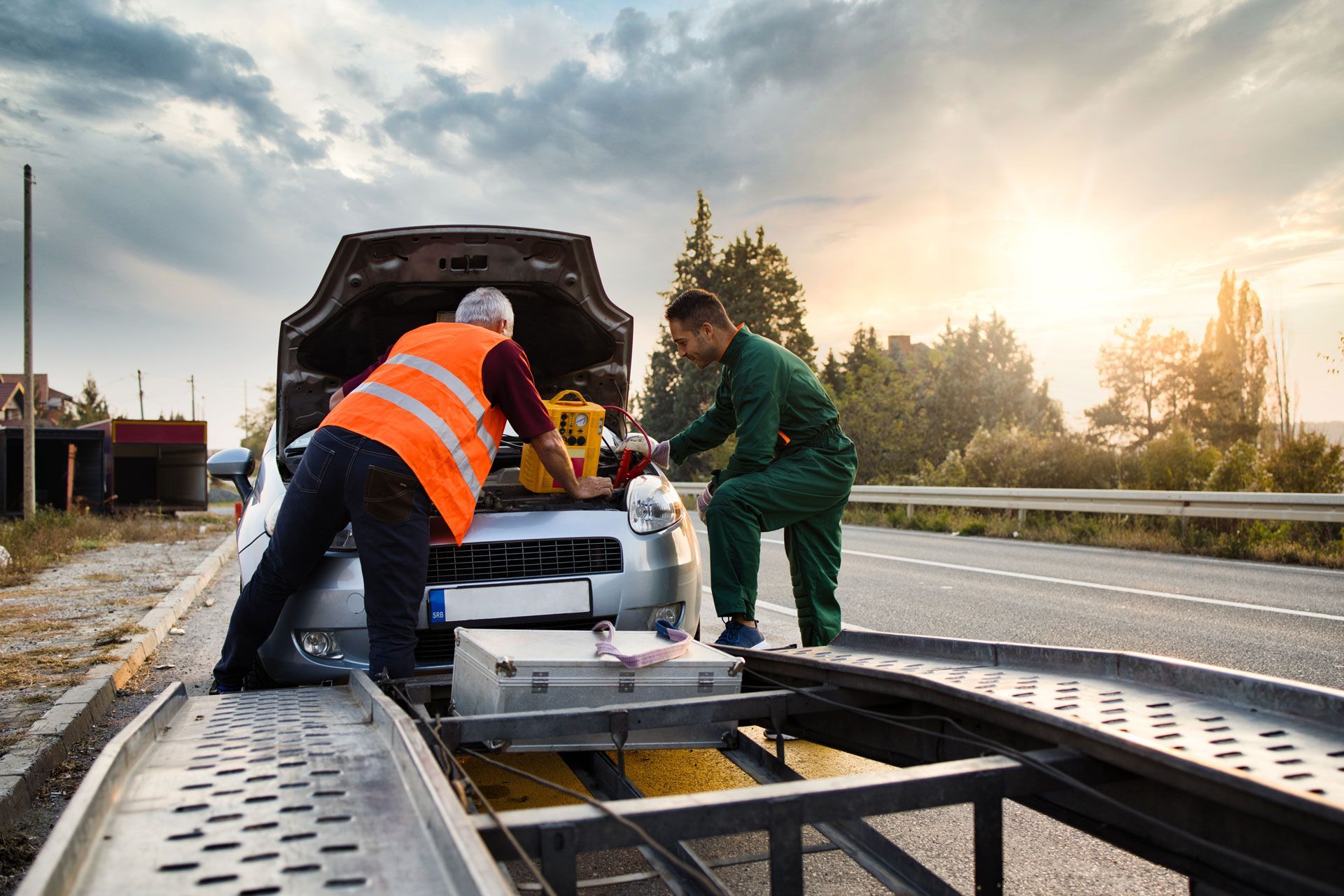 Two people loading a car onto a tow truck on the side of a road.