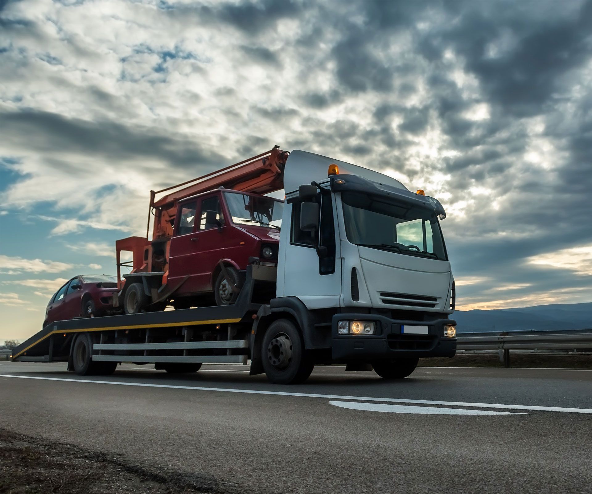 Tow truck hauling two vehicles on a highway under a cloudy sky.