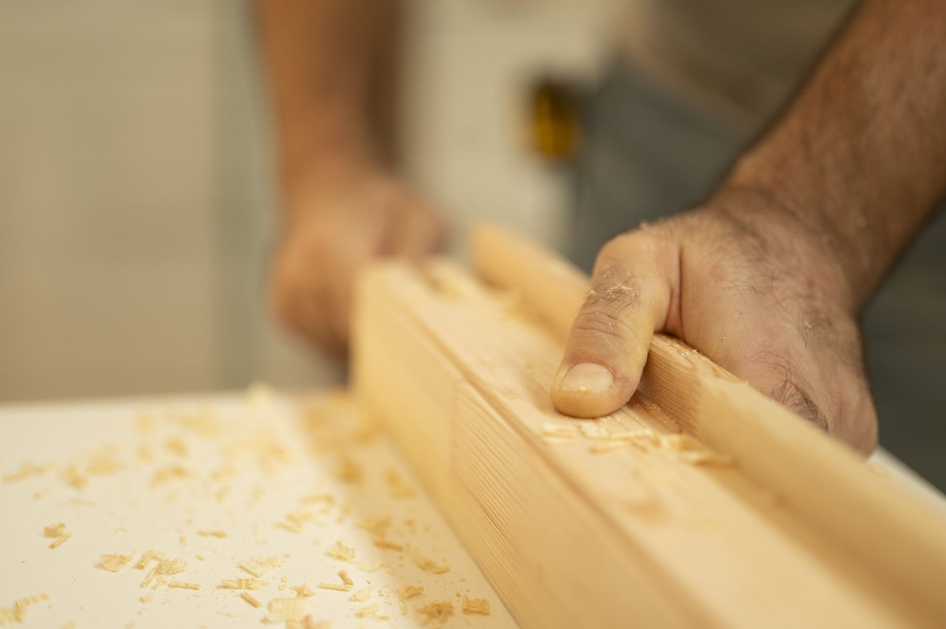 Mani che piallano una tavola di legno, segatura visibile.