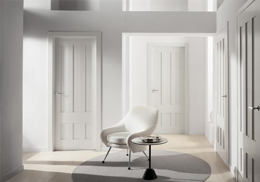 Corridoio bianco con porte, una sedia e un tavolino. Luce naturale da sinistra.