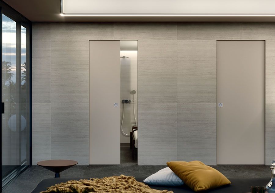 Due porte a filo, di colore chiaro, incastonate in una parete piastrellata.