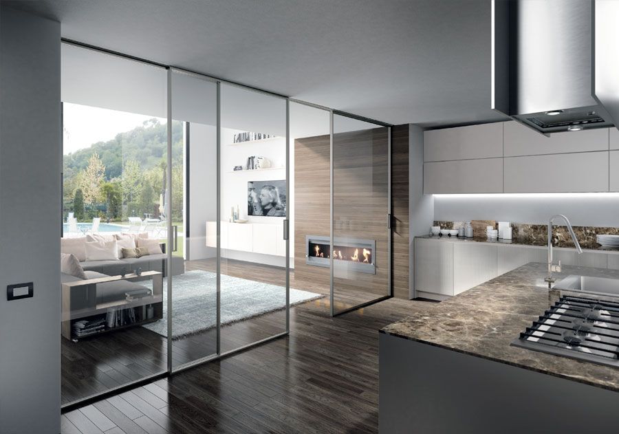 Cucina moderna con porte scorrevoli in vetro che si aprono su una zona soggiorno con vista sull'esterno.