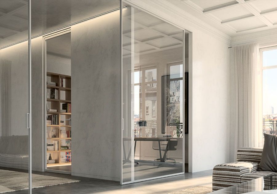 Porte scorrevoli in vetro separano un moderno ufficio dalla zona giorno. La luce del sole filtra all'interno.