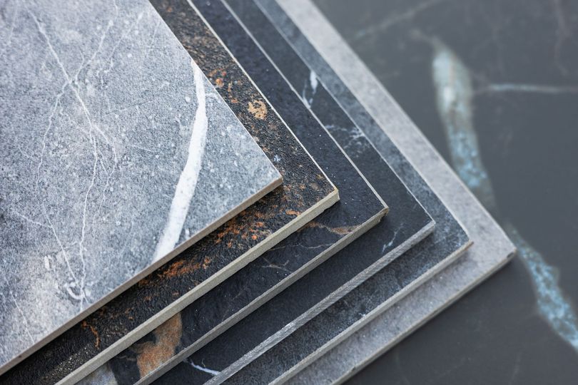 Pila di piastrelle grigie, nere e con motivi marmorei, che presentano diverse texture e design.