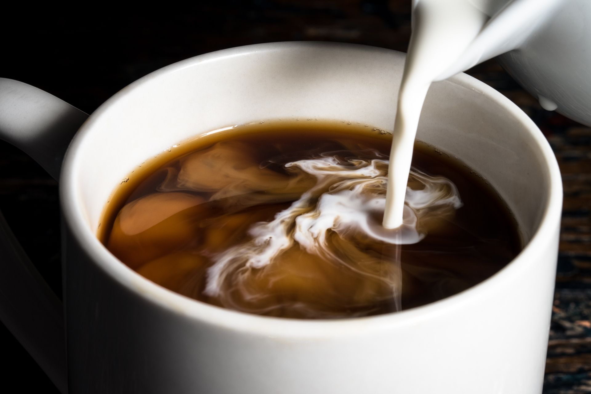 A cup of coffee with milk being poured into it.