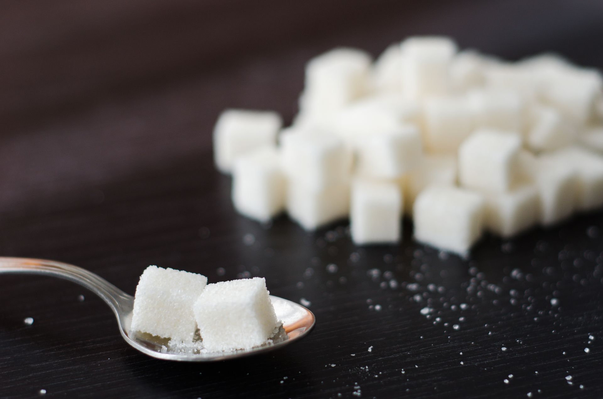 A spoon filled with sugar cubes next to a pile of sugar cubes