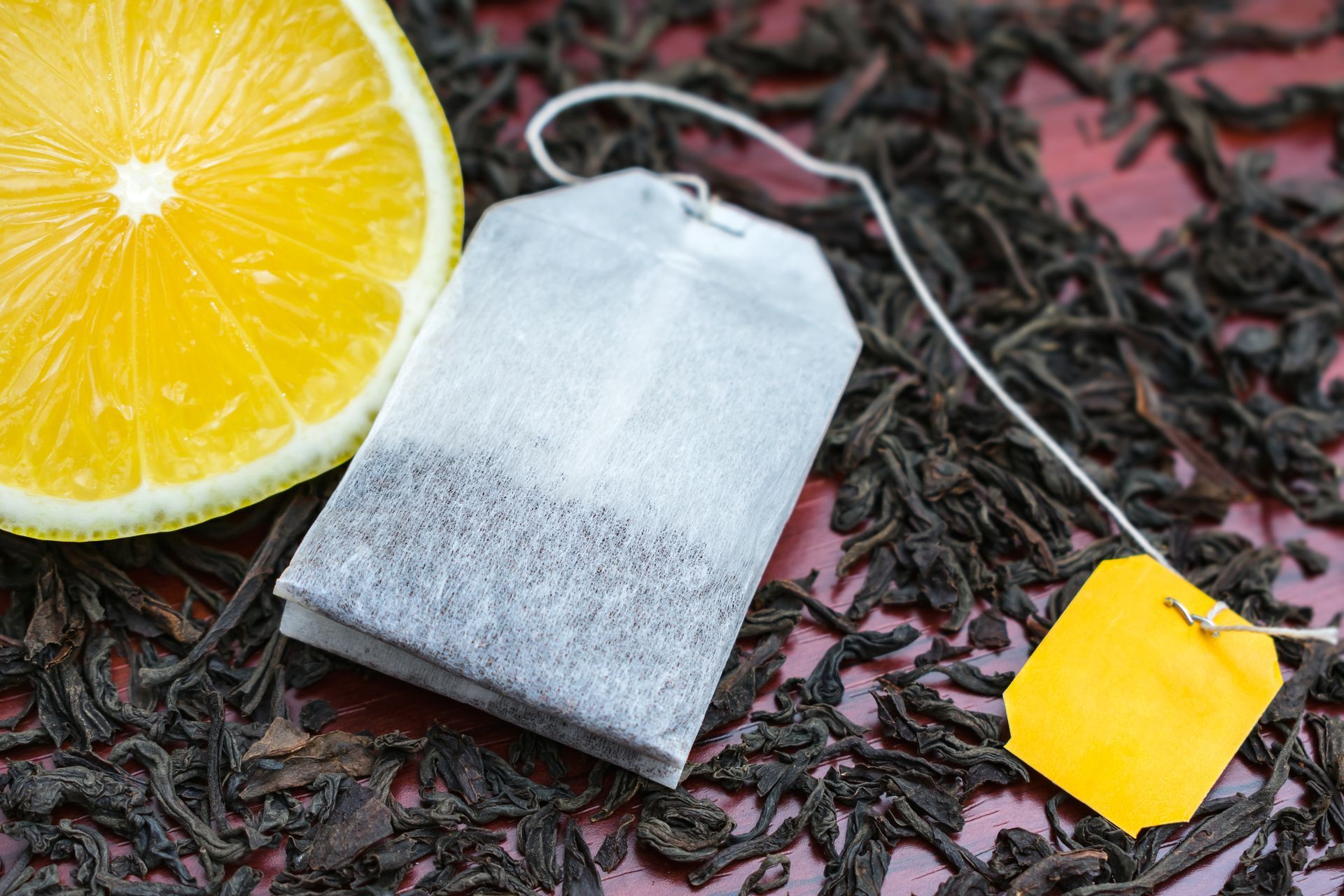 A tea bag is sitting on top of a pile of tea leaves next to a slice of lemon.