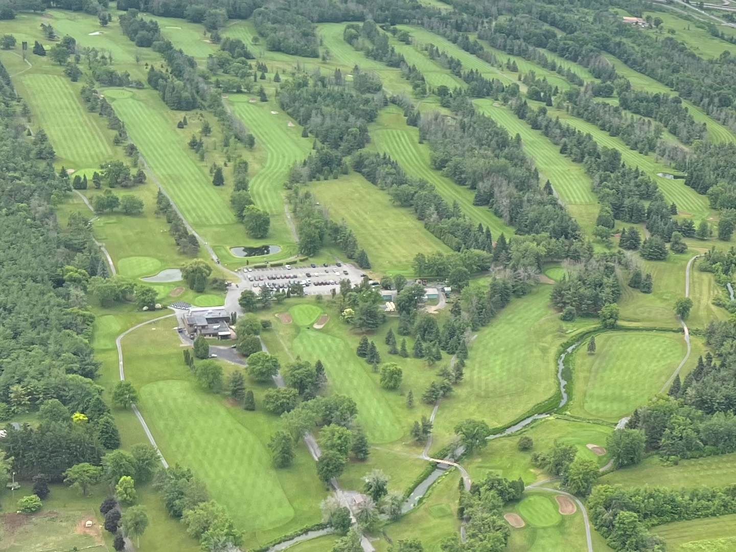 Aerial view of a green golf course with fairways, trees, and a clubhouse.