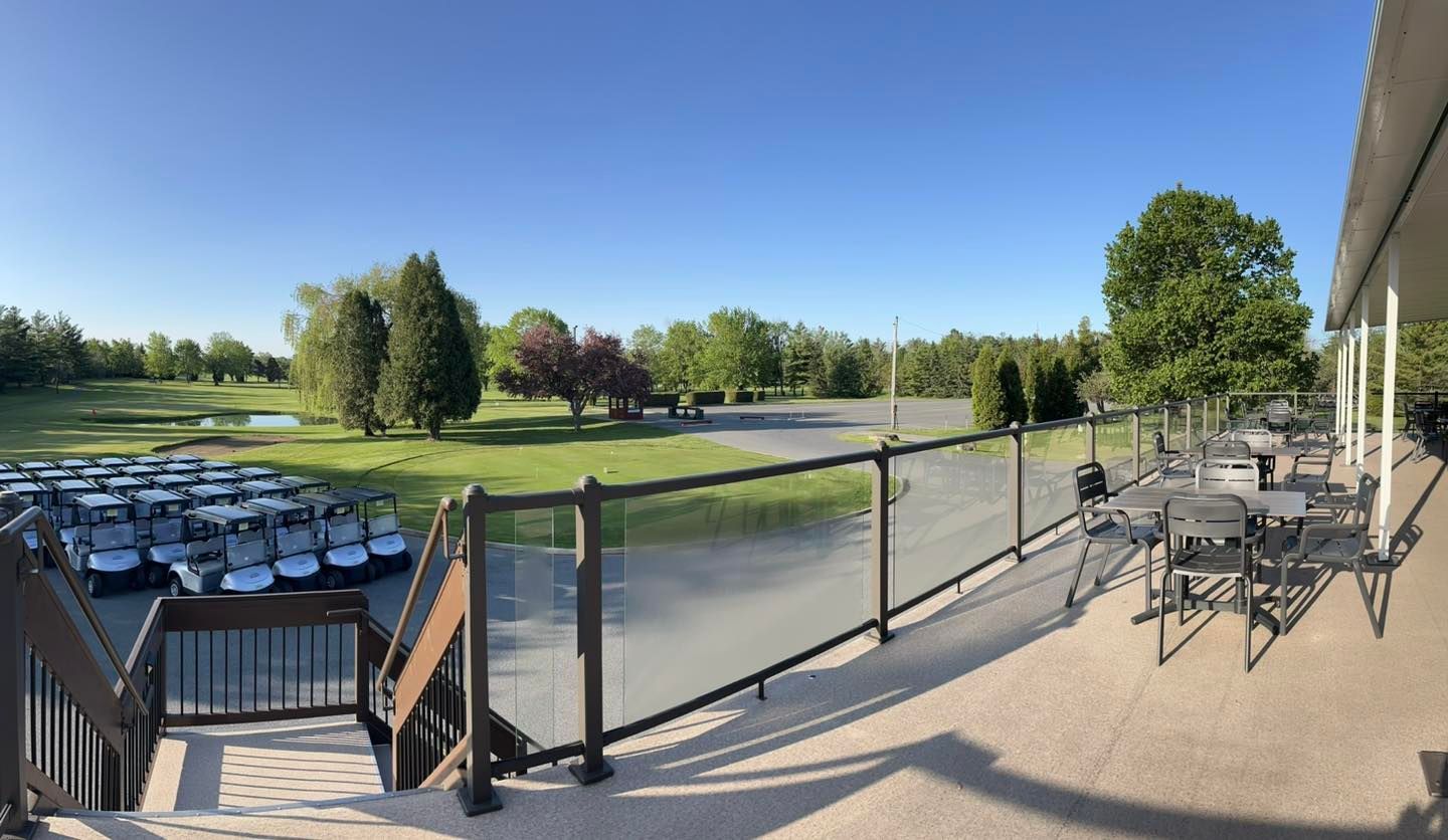 View from a deck overlooking a golf course with parked golf carts and trees under a blue sky.