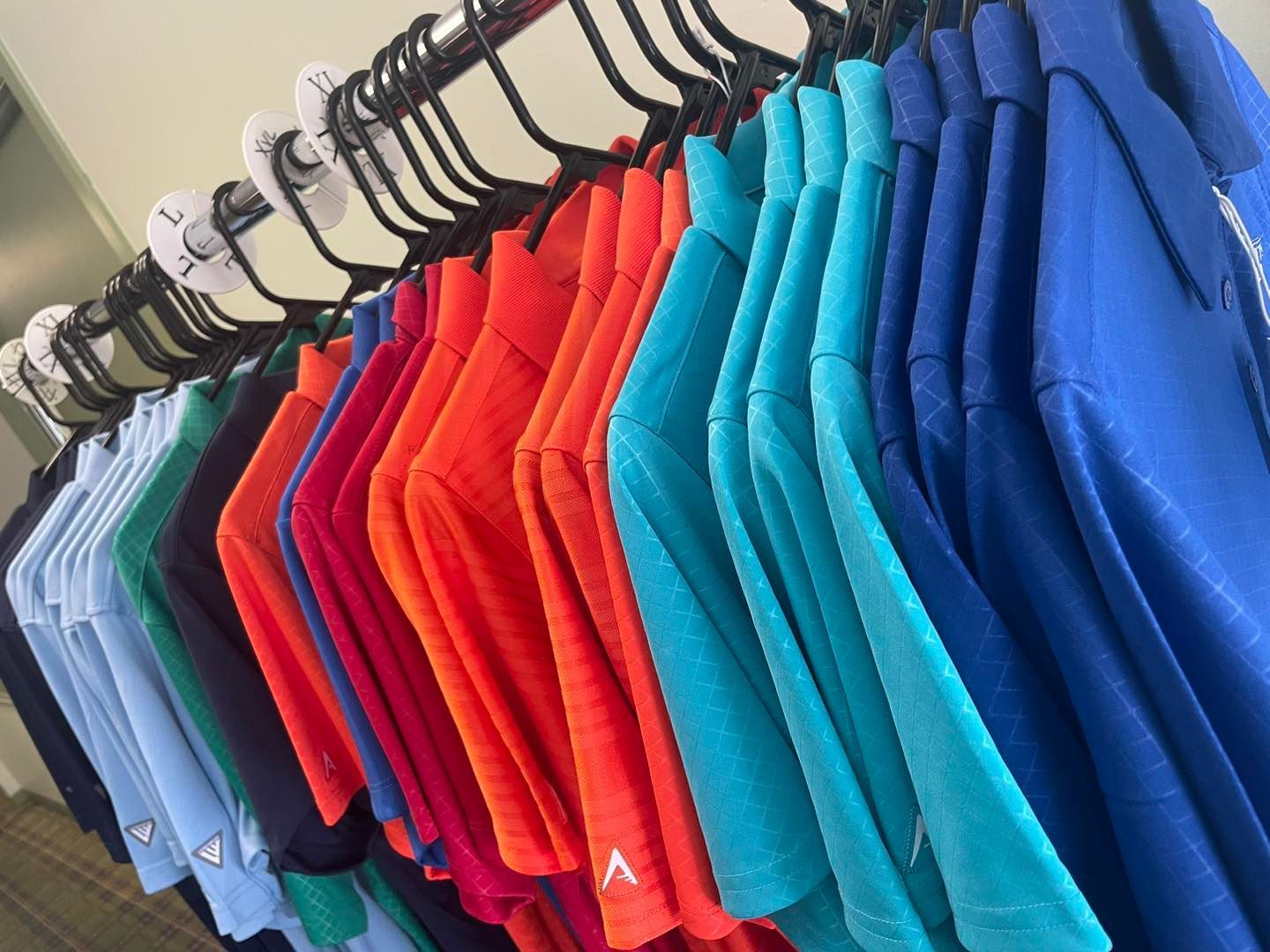 Row of colorful t-shirts hanging on a rack. Various hues include blue, red, orange, and teal.