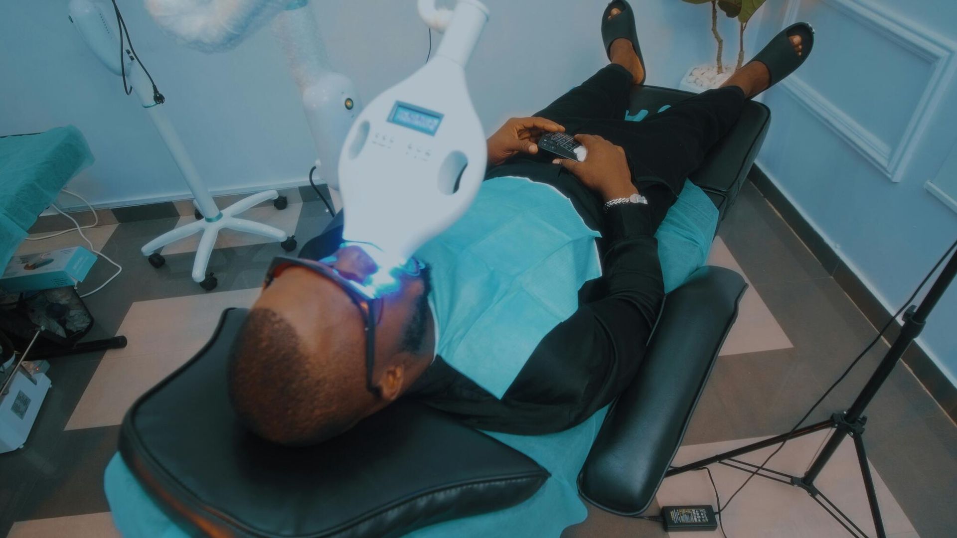 Man undergoing teeth whitening treatment, lying in dentist chair, blue light focused on his mouth.