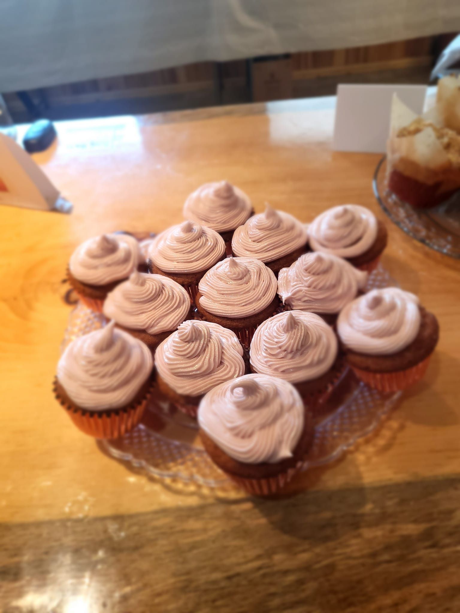 A plate of cupcakes with pink frosting on a wooden table.