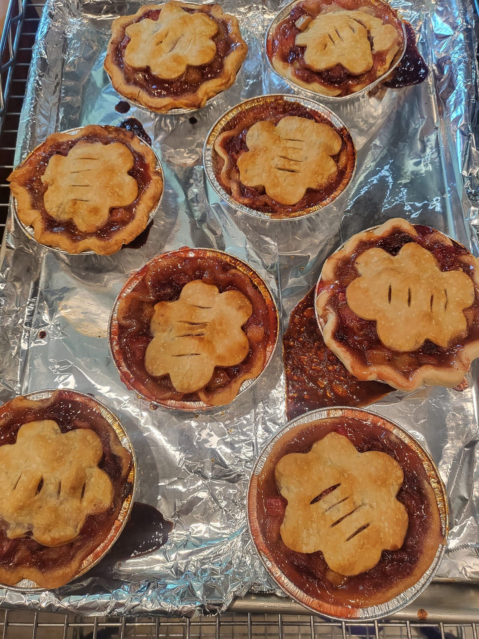 A bunch of mini pies are sitting on top of a tin foil tray.